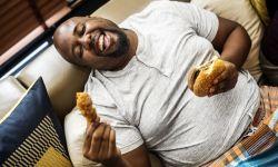 Uomo sovrappeso mangia sul divano